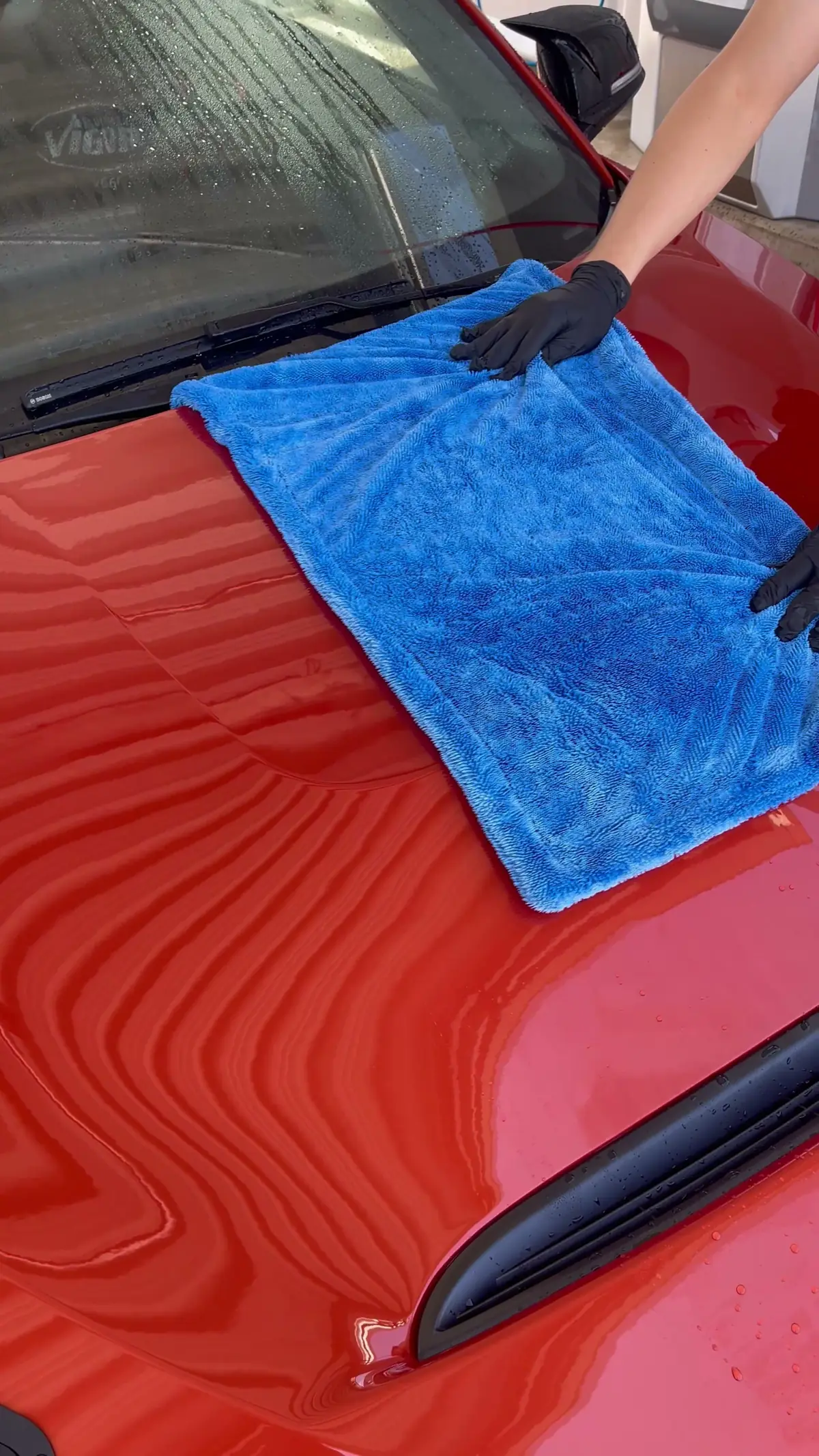 Motorhaube eines BMW 140 wird mit einem Mikrofasertuch getrocknet, dahinter die Frontscheibe