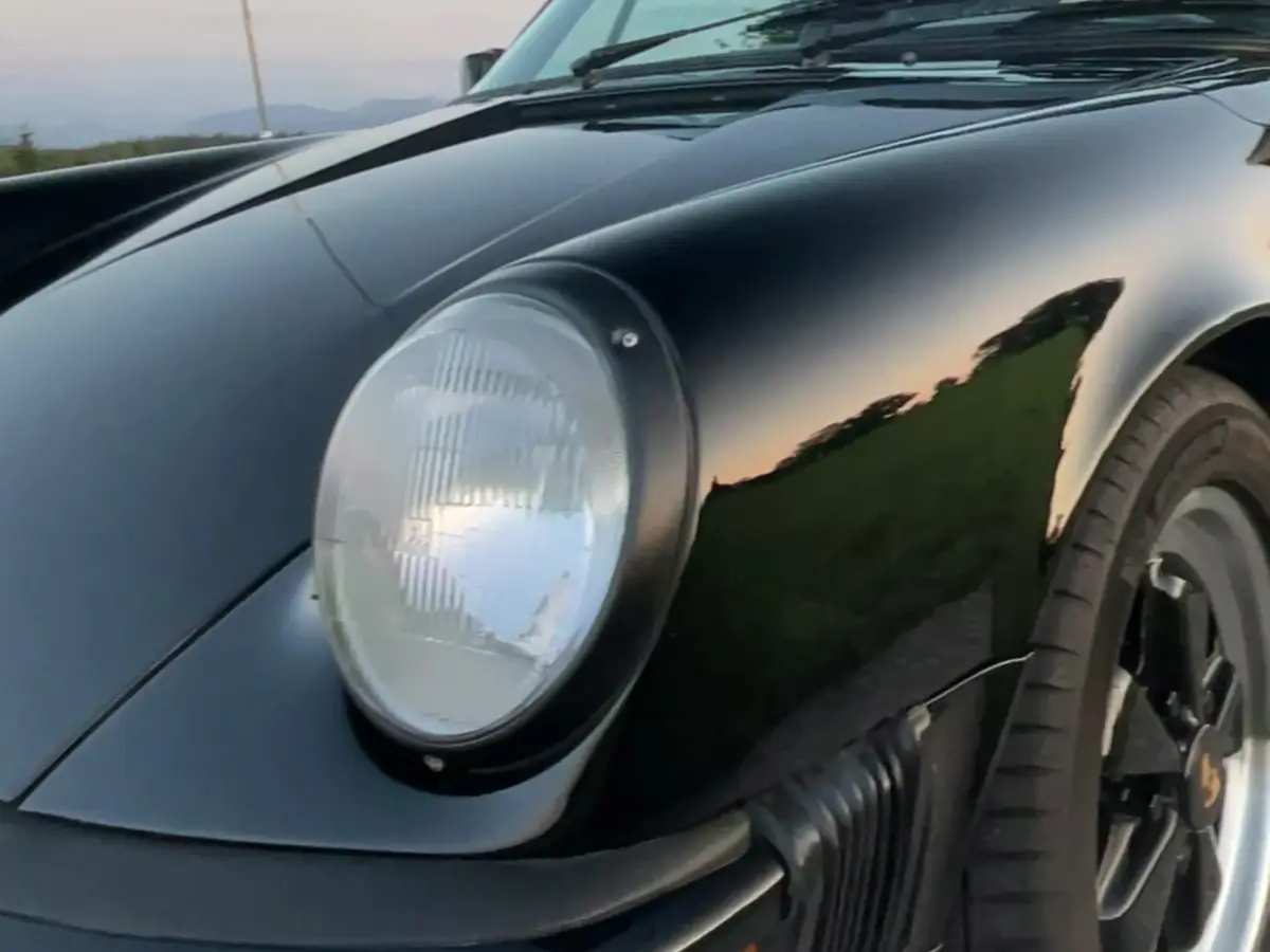 Scheinwerfer und Vorderrad eines schwarzen Porsche 911 im Abendlicht