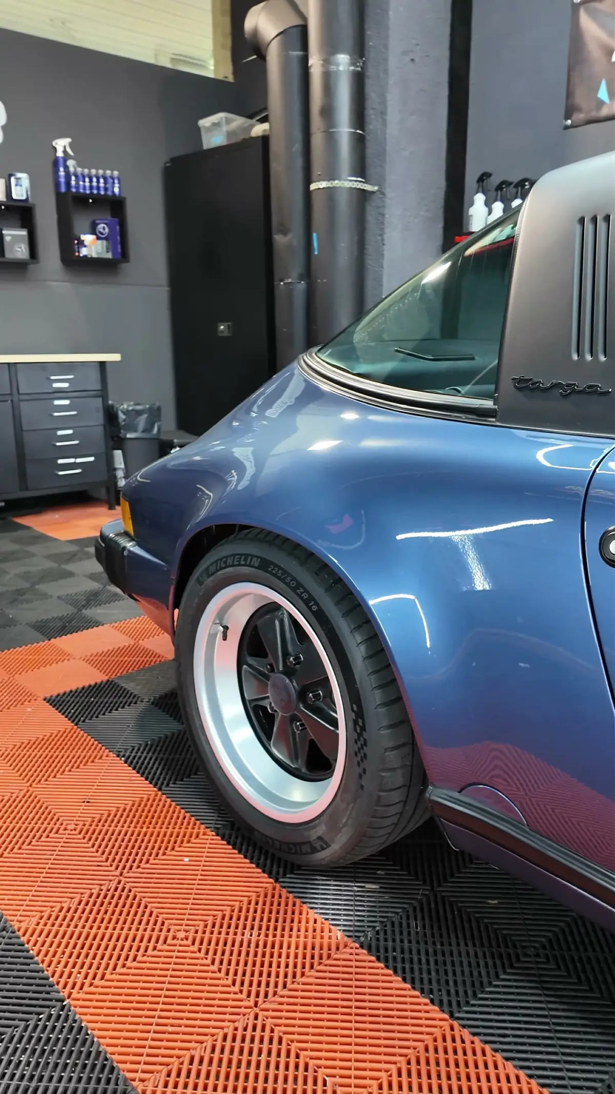 Hinterrad eines blauen Porsche 911 Targa auf dem orangen Werkstattboden