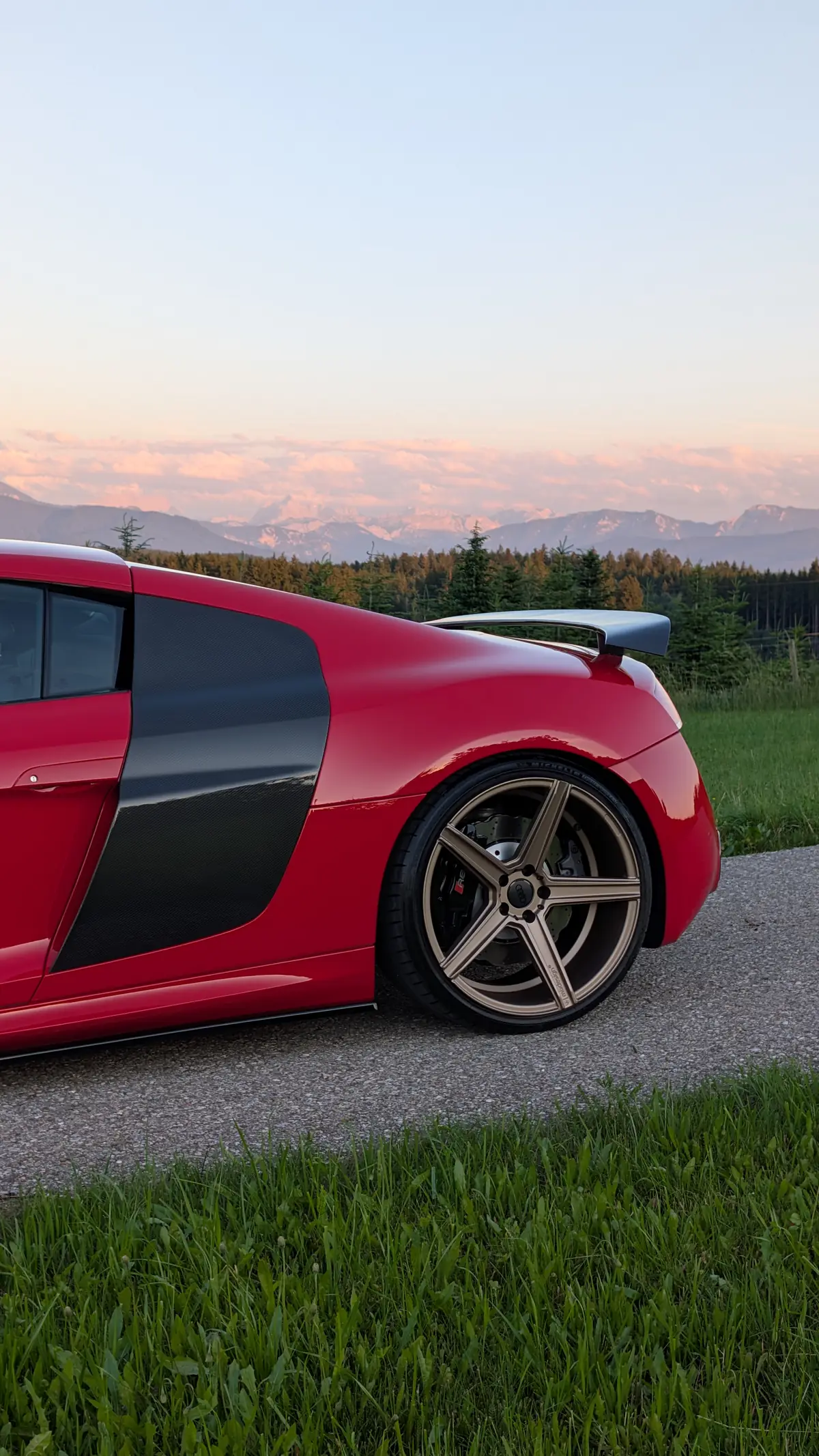 Seitenansicht eines roten Audi R8 mit bronzefarbenen Felgen vor den Alpen