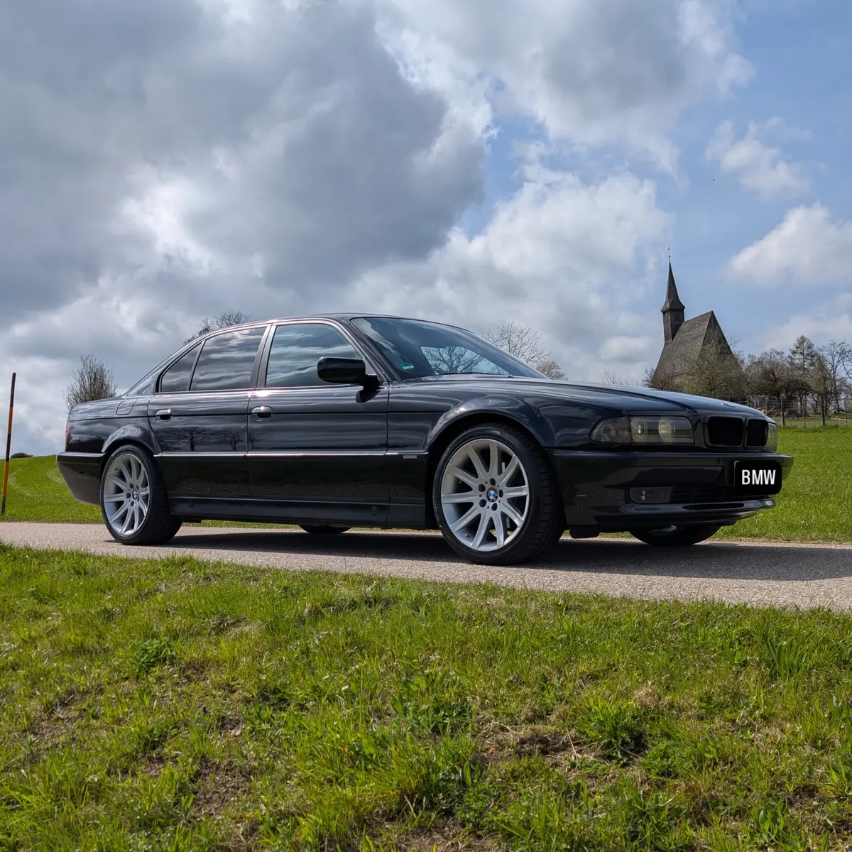 Dunkler BMW 7er vor einer Wiese mit Kirche im Hintergrund